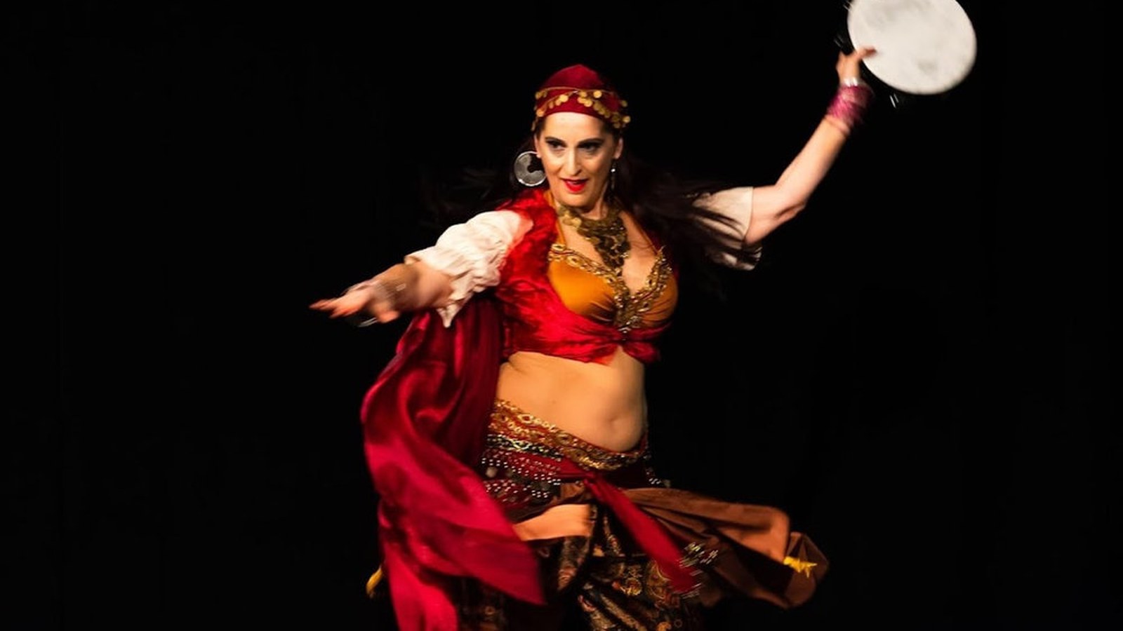 Bea Azahar performing authentic belly dance solo on stage in red and gold costume with frame drum