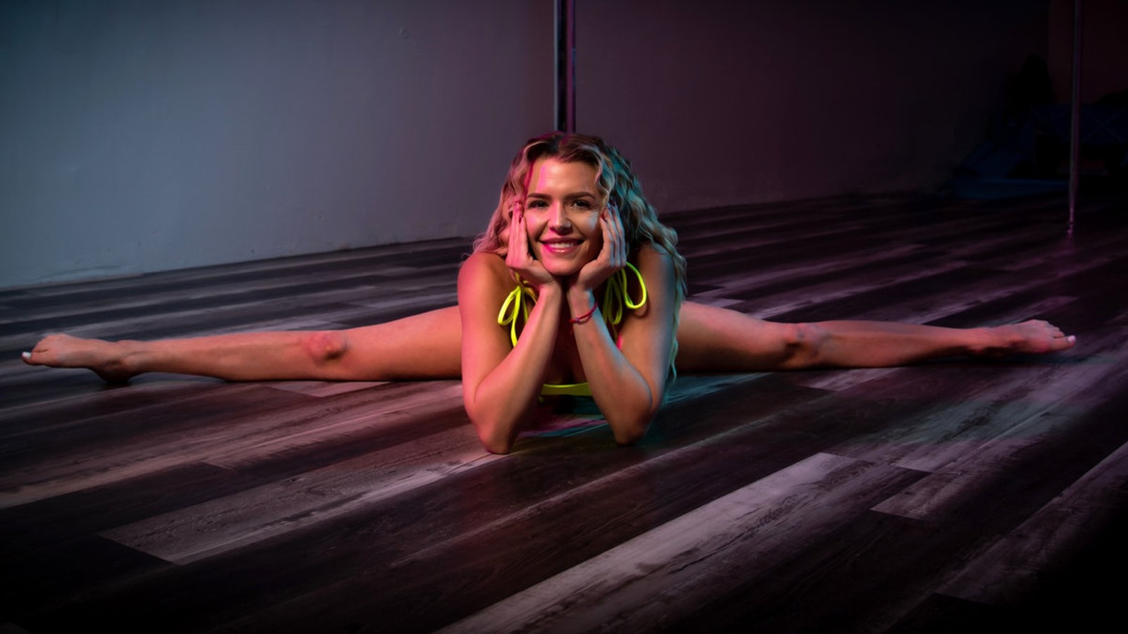 Vertical Addicts instructor stretching on the studio floor with dance poles visible behind