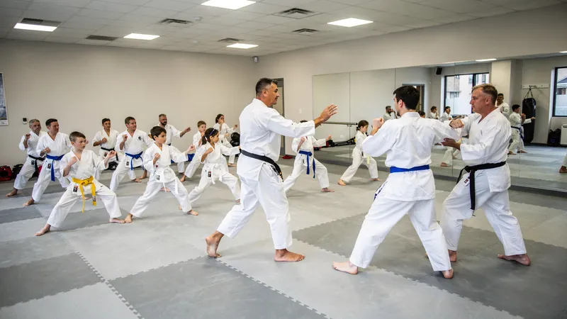 Children and adults in white gis practicing martial arts techniques in a dojo with instructor leading the class