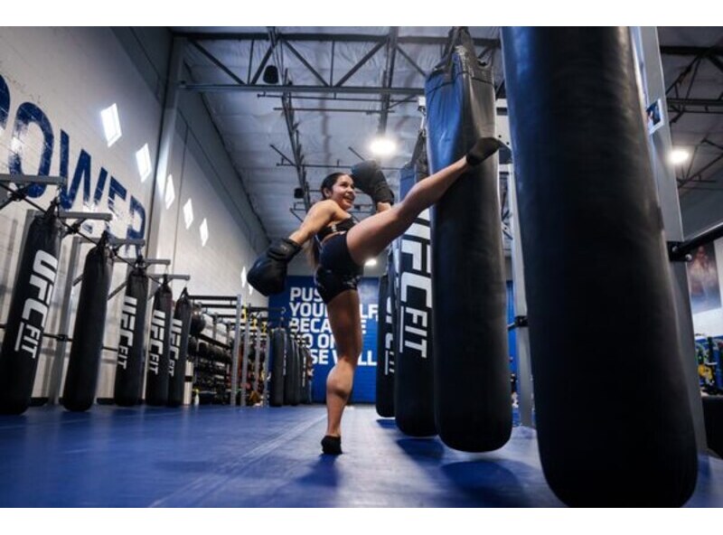 Woman practicing kickboxing on a heavy bag inside a UFC FIT training facility.