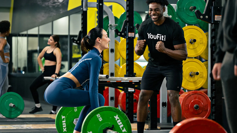 YouFit coach guiding a member during a strength-training exercise.
