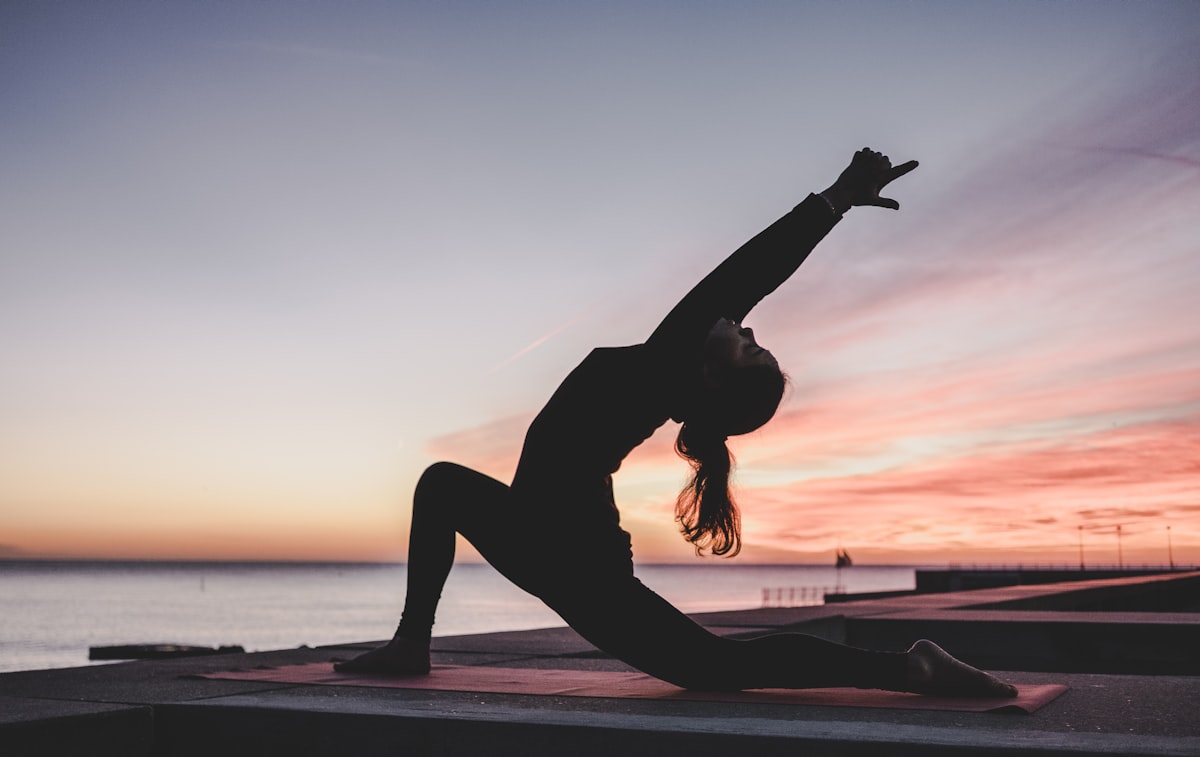 Woman practicing yoga in a bright modern studio with floor-to-ceiling windows overlooking tropical plants and warm afternoon light